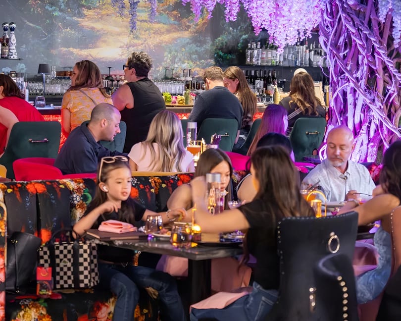 Diners enjoying a vibrant restaurant interior with floral decor, a bar, and colorful seating.